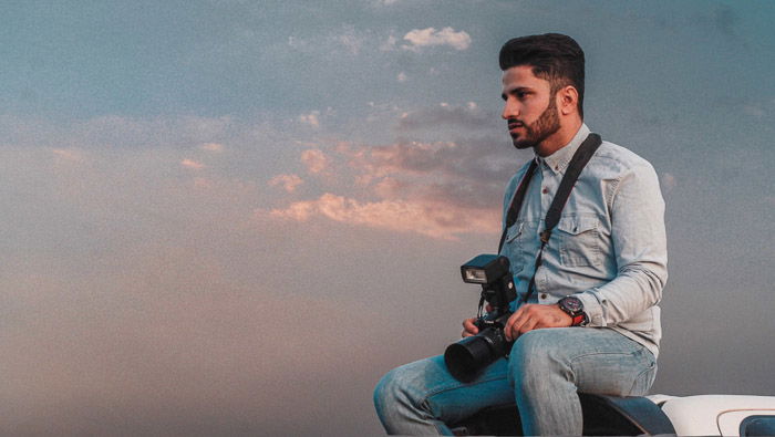 A photographer sitting on top of a car, contemplating a shot