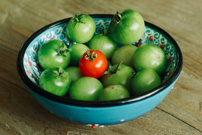 A bowl of green tomatoes with one red tomato