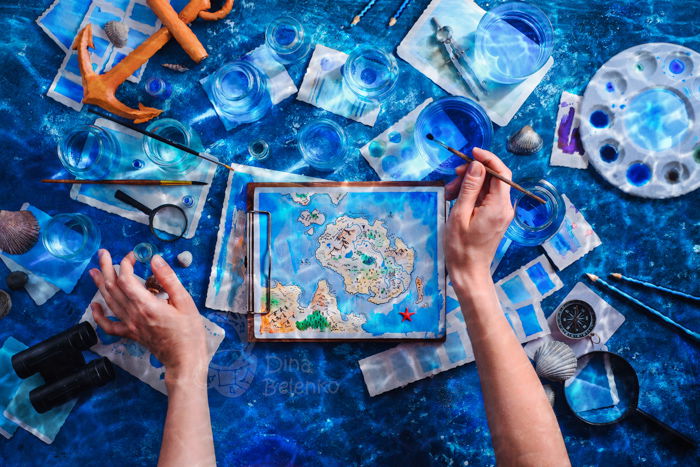 An overhead shot of a persons hands, painting a map underwater 