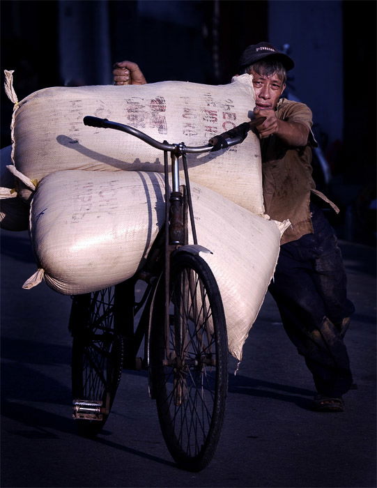 A street portrait of a man carrying large bags of rice on a bicycle