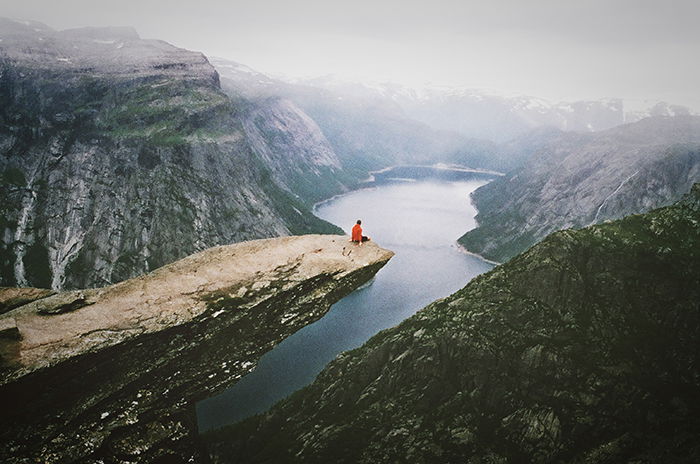 A candid photography example ofa person sitting on a cliff overlooking a stunning mountainous landscape 