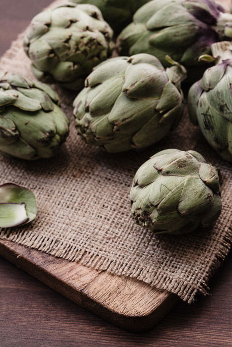 A close up of artichokes on a rustic burlap and wooden background