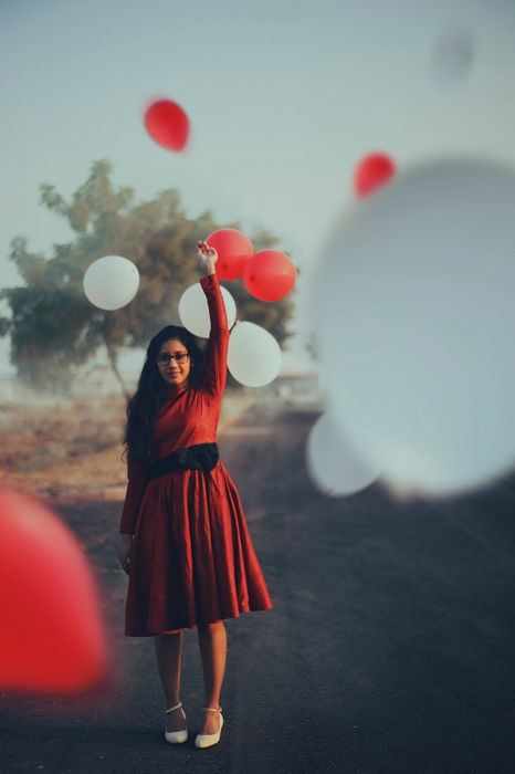 A portrait of a girl in a red dress standing among floating red and white balloons - photo booth ideas