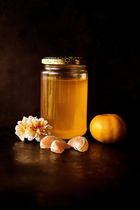 Rustic still life photo of a jar of honey, mandarin segments and flowers against a dark background - photography assignments