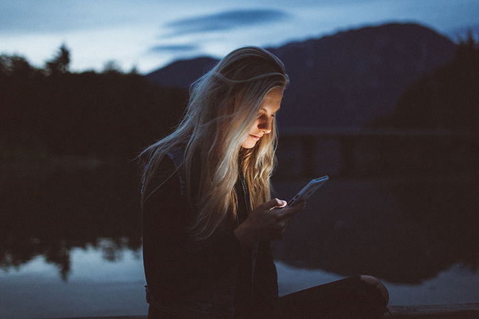 A portrait of a blonde haired woman using her smartphone outdoors in low light