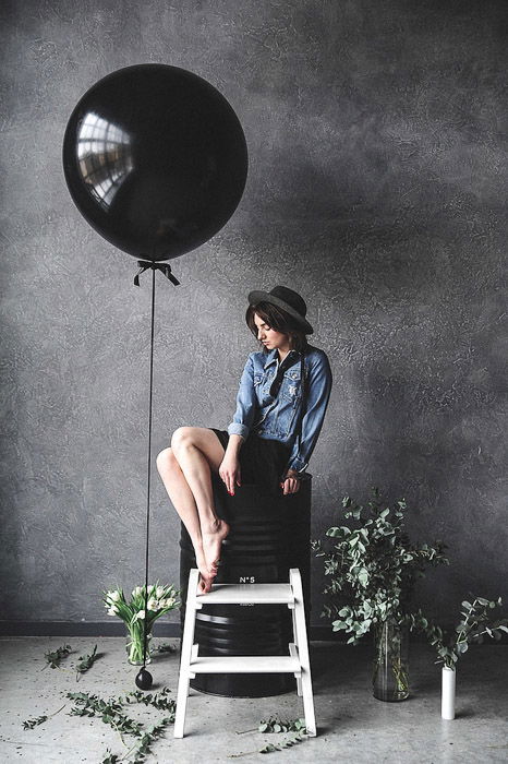 A female model posing by a large black balloon in a photography studio- photography internships