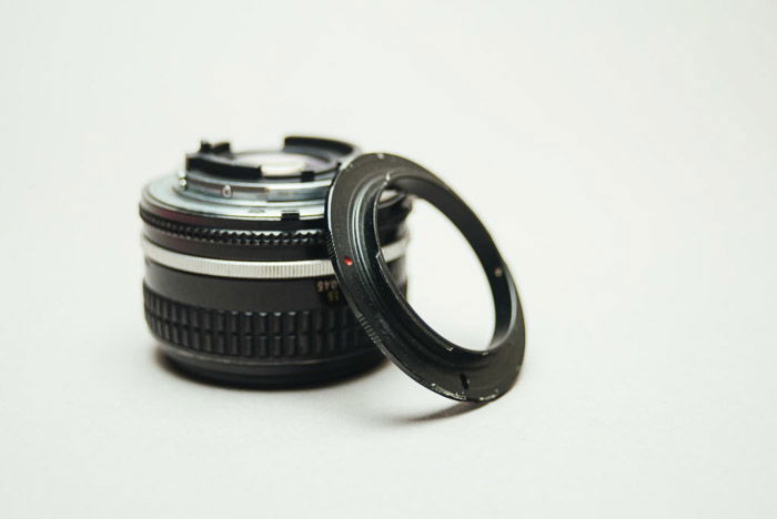 A camera lens beside a reversing ring on white background