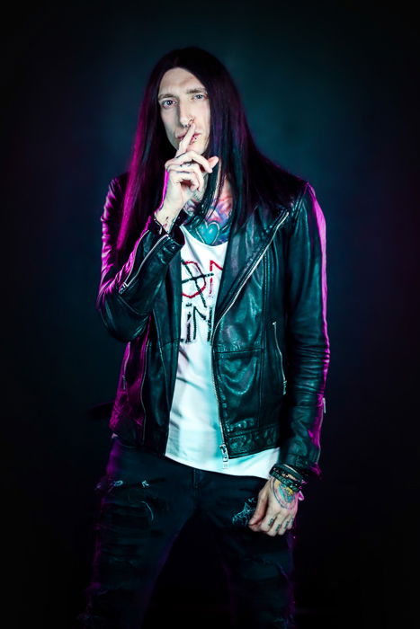 A portrait of a long haired male photography model posing against a dark background