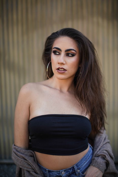 A portrait of a brunette female model posing by a brick wall