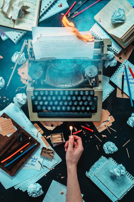 A creative writer themed still life featuring a typewriter, crumpled paper, a hand holding a match and text in photography