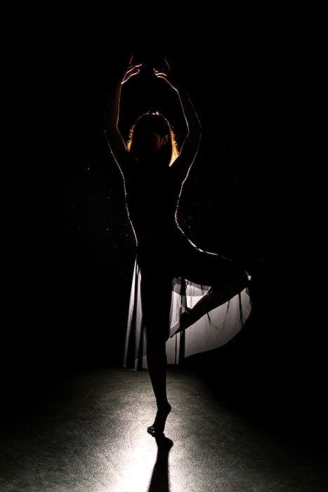 A beautiful ballet photography shot of a female dancer posing onstage in low light