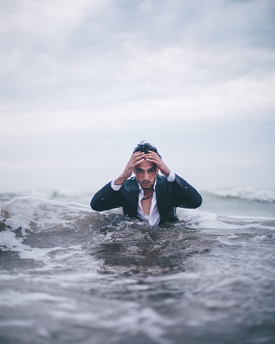 A dramatic conceptual portrait of a man emerging from the sea with his hands on his head - conceptual photography ideas