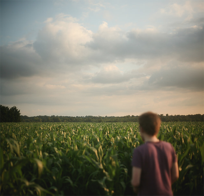 A blurry image of a person in a field with plants with their back to the camera by fine art photographer Luke Sharrat