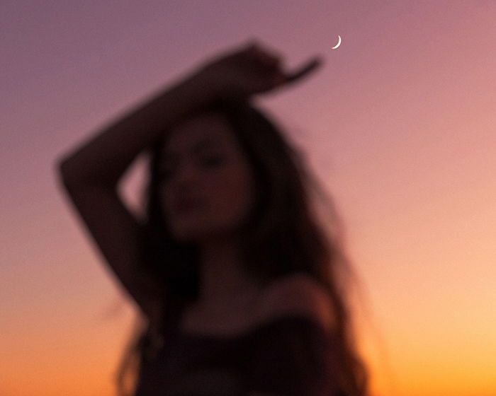 Dreamy, blurry portrait photo of a woman pointing at the sliver of the moon by fine art photographer Mike Monaghan