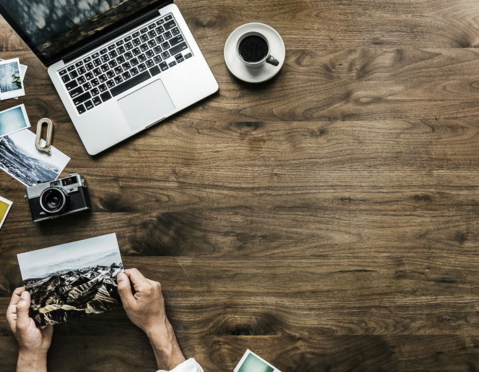 An overhead shot of a laptop, coffee and a person looking at photos