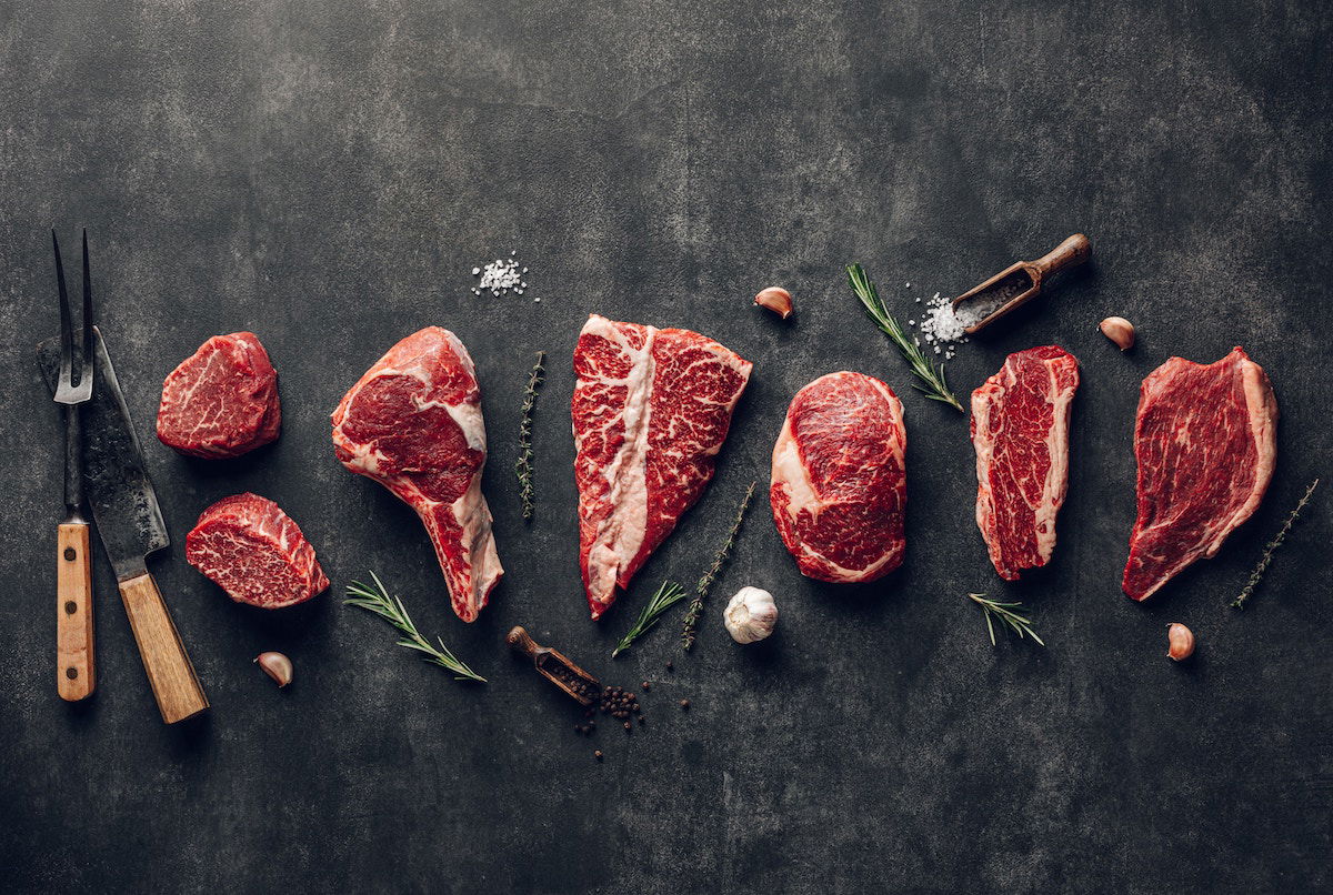 An overhead flat lay of steak ingredients and kitchen utensils spaced nicely