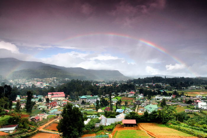 A beautiful landscape with a full bow of the rainbow above - rainbow photography tips