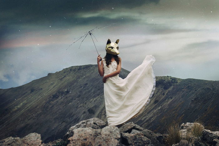 a conceptual portrait of a female model in a wolf mask standing in a mountainous landscape