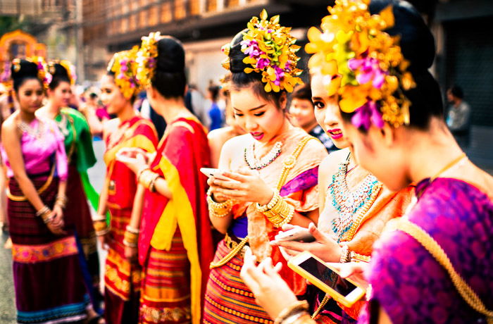 A street portrait of girls checking their smartphones before the start of the annual flower parade in Chiang Mai, Thailand. Photos that tell a story