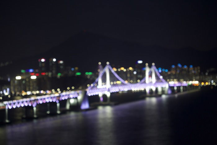 A blurry out of focus image of an illuminated bridge over a city river at night 