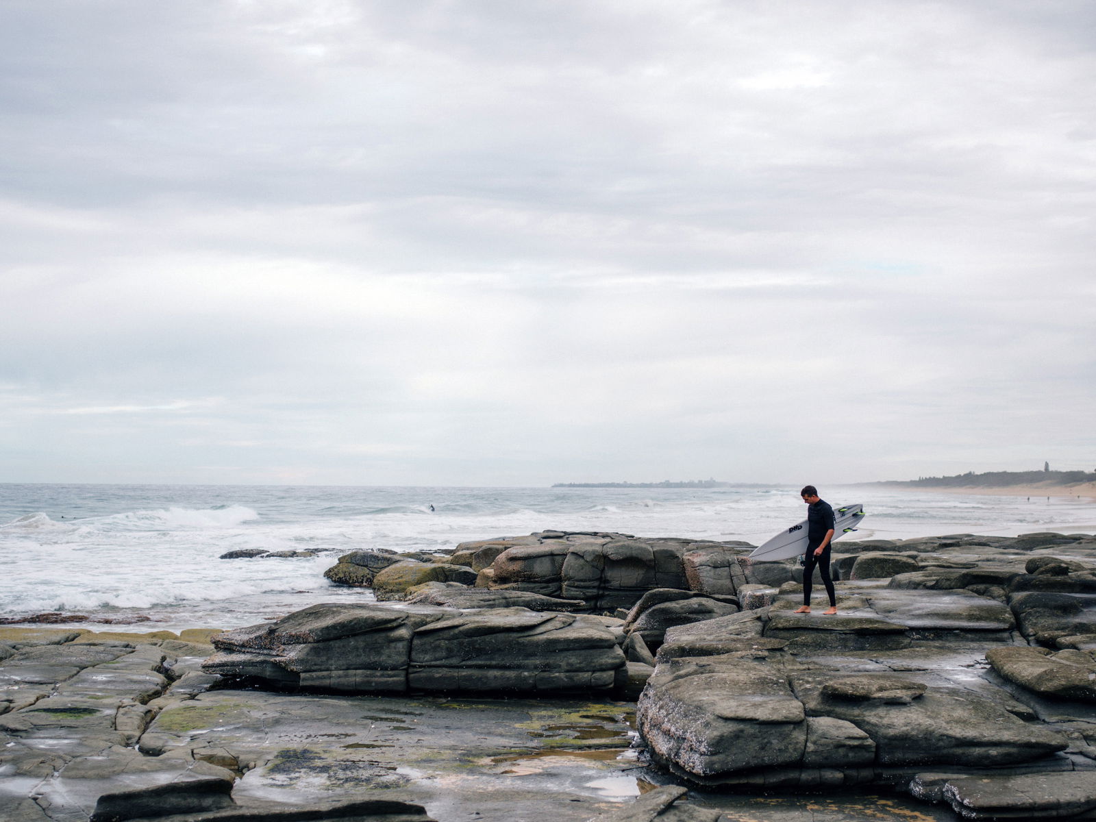 How to Do a Bend and Warp Trick in Photoshop - a surfer walking on rocks by the coast