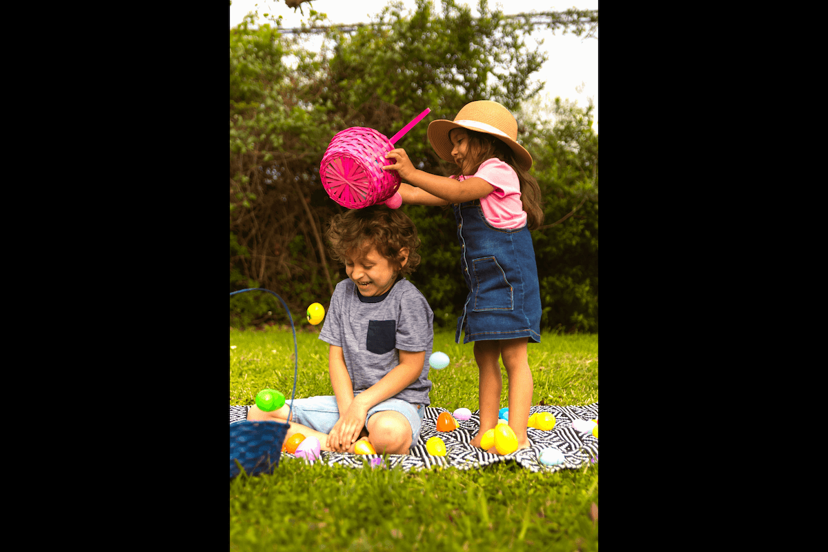 A candid of a girl dumping plastic eggs over a boy and them both laughing as an example of candid Easter picture ideas