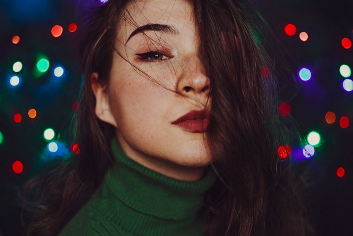 A woman with a thoughtful gaze, wearing a green turtleneck and standing in front of colorful lights. 