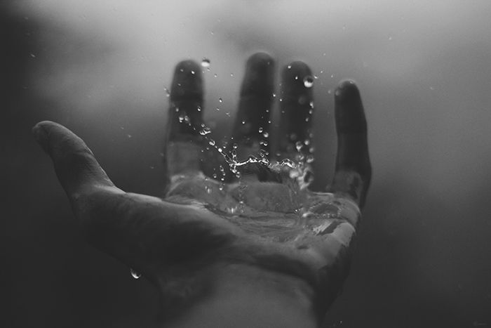 A hand with droplets of water falling off it, set against a misty background. 