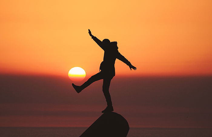 The silhouette of a person balancing on a pink in front of a beautiful sunset