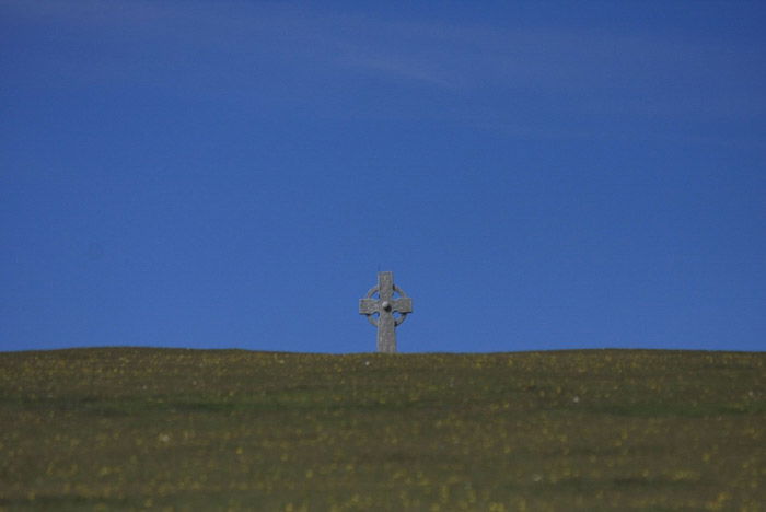 A minimalist landscape photography shot featuring a stone cross under a clear blue sky