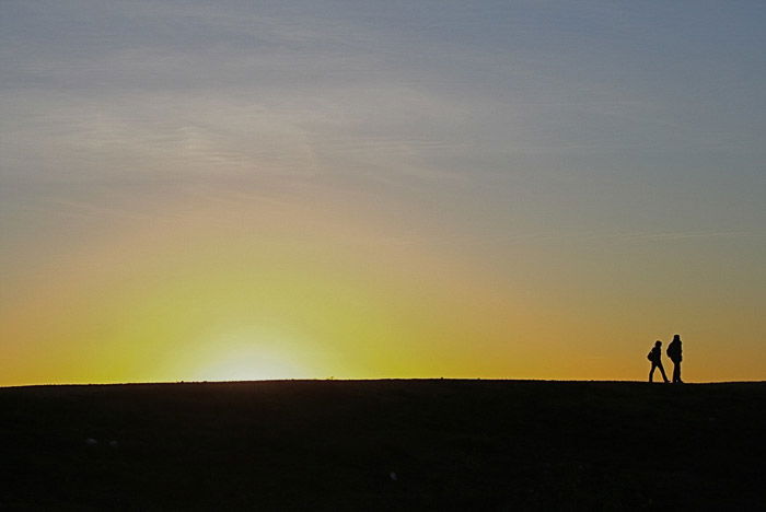 Silhouettes of two people walking through a minimalist landscape at sunset