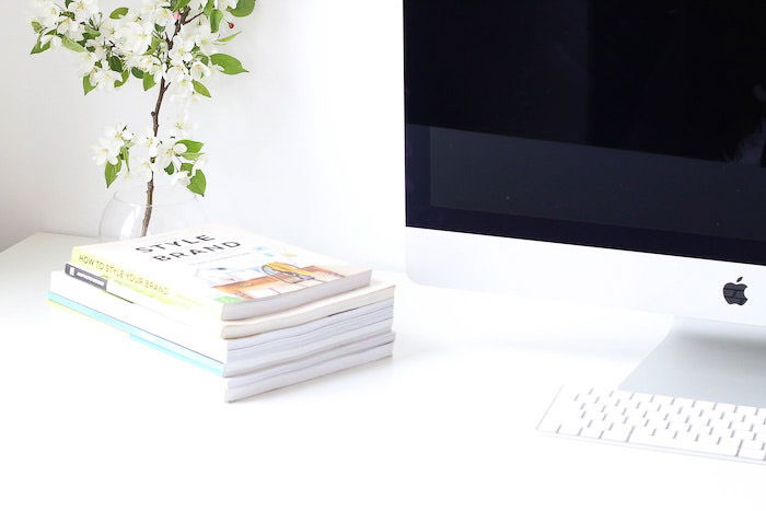 A bright and airy shot of a photographers home office with computer, plant, and stack of books