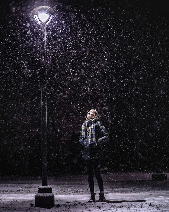 Atmospher winter portrait of a female model posing under falling snow at night