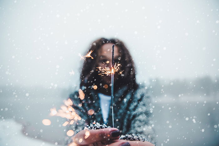 Atmospher winter portrait of a female model posing with sparklers under falling snow at night