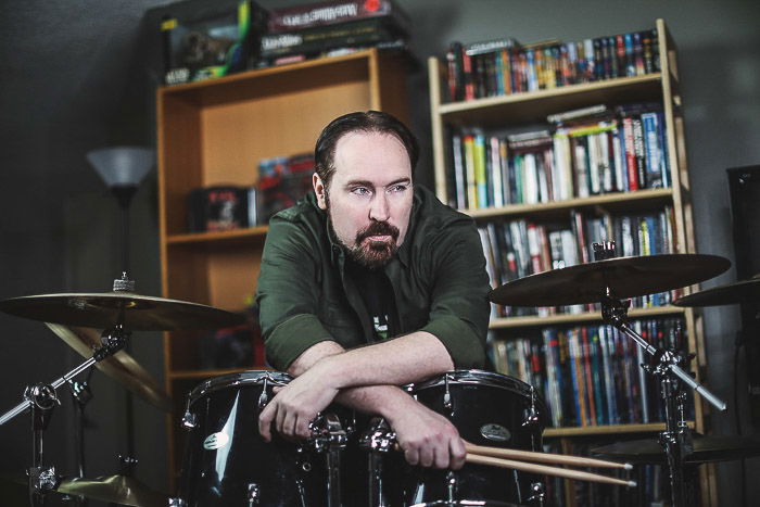 A portrait of a man posing by a drum kit shot with studio lights