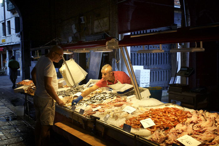 A man interacting with a market vendor at a fish market in Venice - Italy pictures