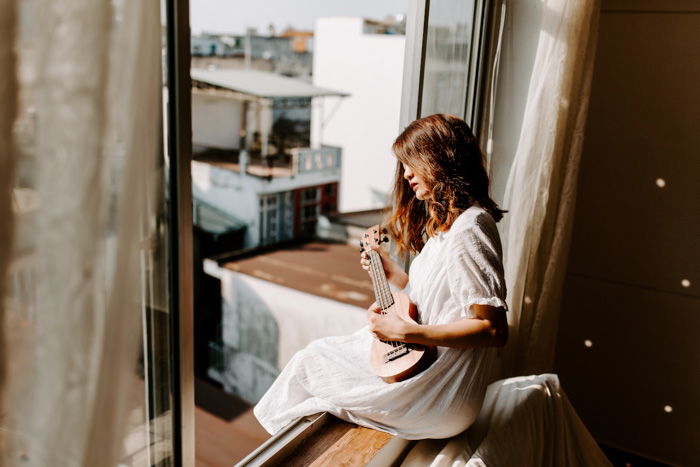 Bright and airy portrait of a female model sitting in a window with a guitar