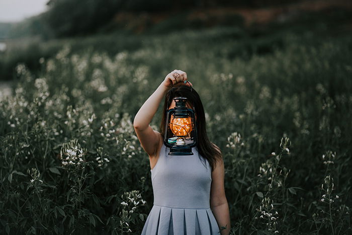 An outdoor portrait of a female holding a lantern with fairy lights in front of her face.