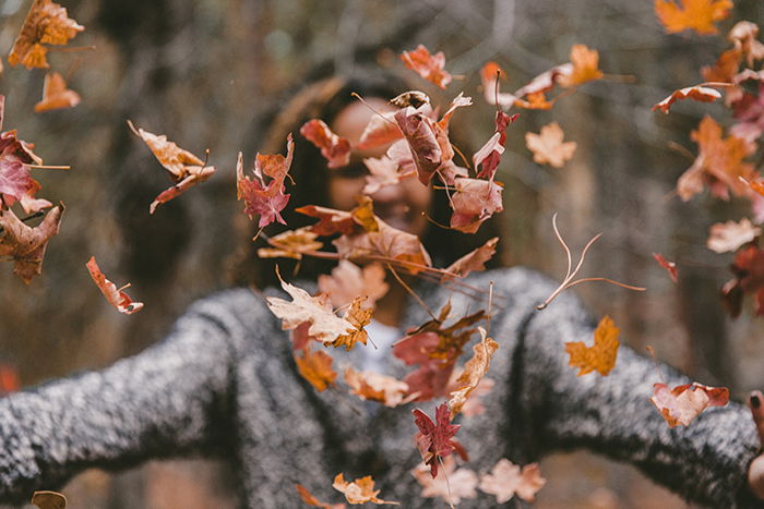 Autumn photography of thrown leaves in the foreground with a blurred female in the background