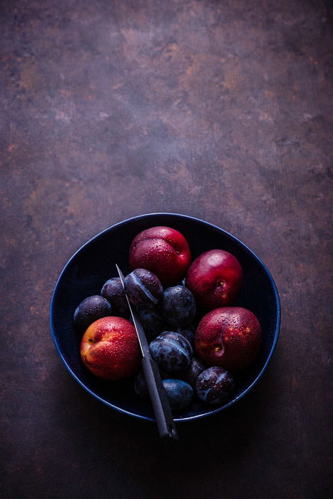 Dark and moody fruit photography of plums in a bowl