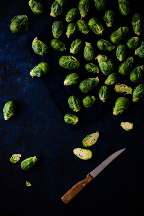 A dark and moody flatlay of Brussels sprouts on dark blue background