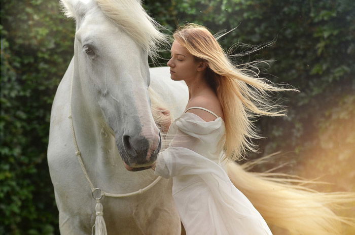 A dreamy photo of a female model with long blond hair posing beside a white horse after using Photoshop overlays 