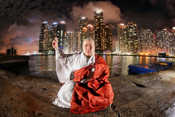 Conceptual urban portrait of a monk meditating in front of a night cityscape