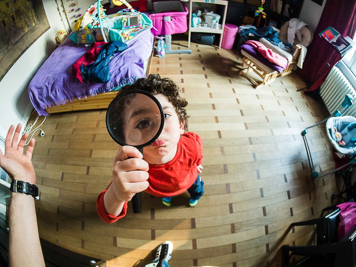 A typical funny fisheye portrait of a little boy holding a magnifying glass towards the camera