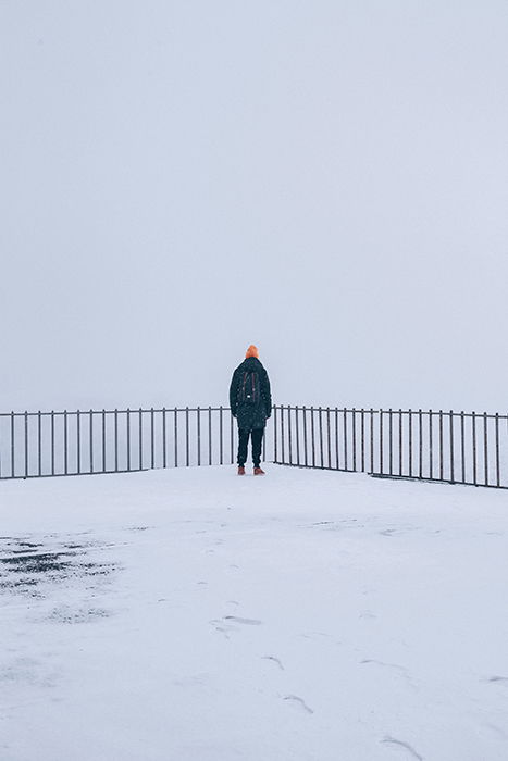  A snowy winter portrait of a figure standing by a fence