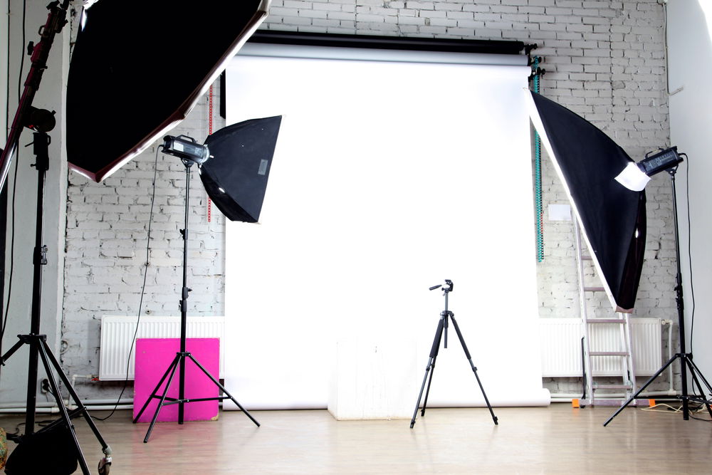 A photographic studio with lighting equipment and backdrop, including tripods and camera supports. 