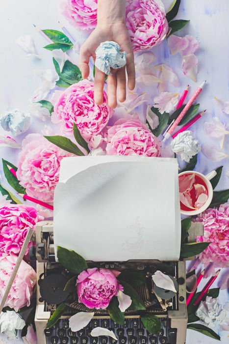 Cool still life featuring roses, a typewriter and a hand holding crumpled paper as an example for spring photography ideas