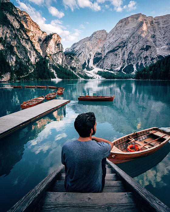 A person sitting on a dock surrounded by many boats and looking out over a lake.