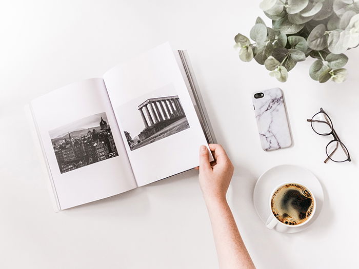 An artistic flatlay of a cool photobook, a coffee cup, glasses and a smartphone on a white table - how to make your own photo book to make your own photo book