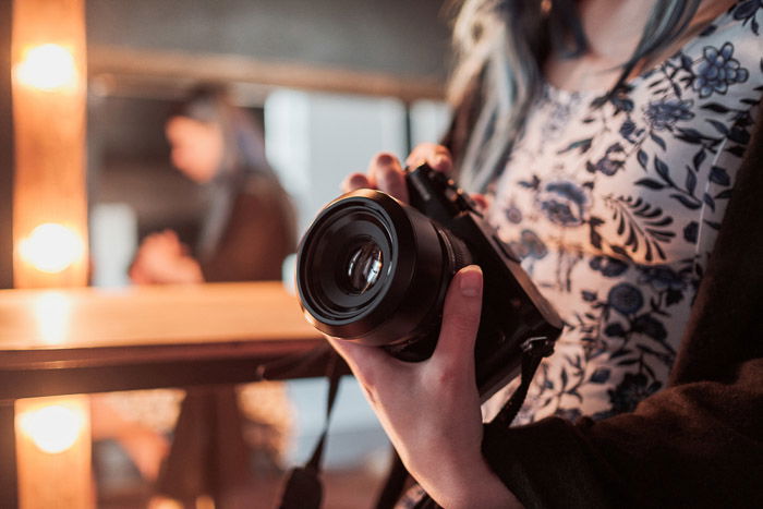 A candid shot of a woman holding a DSLR camera indoors